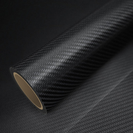 Rouleau de vinyle carbone noir brillant posé sur une feuille du même vinyle